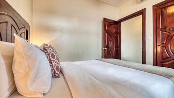A hotel room with a bed, pillows, a wooden door, and an air conditioning unit.