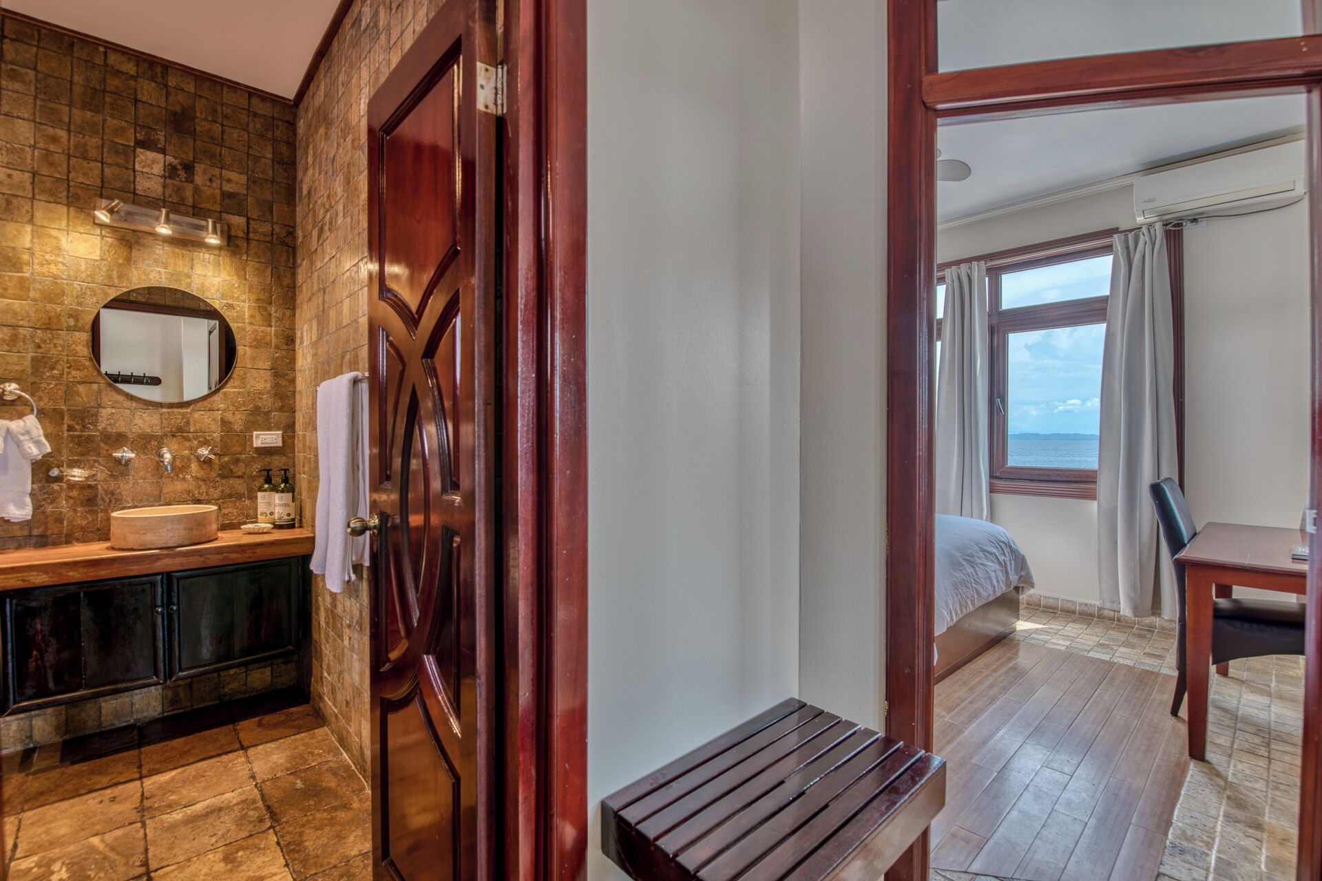 A bathroom with a wooden door, a round mirror, a sink, and a towel rack.