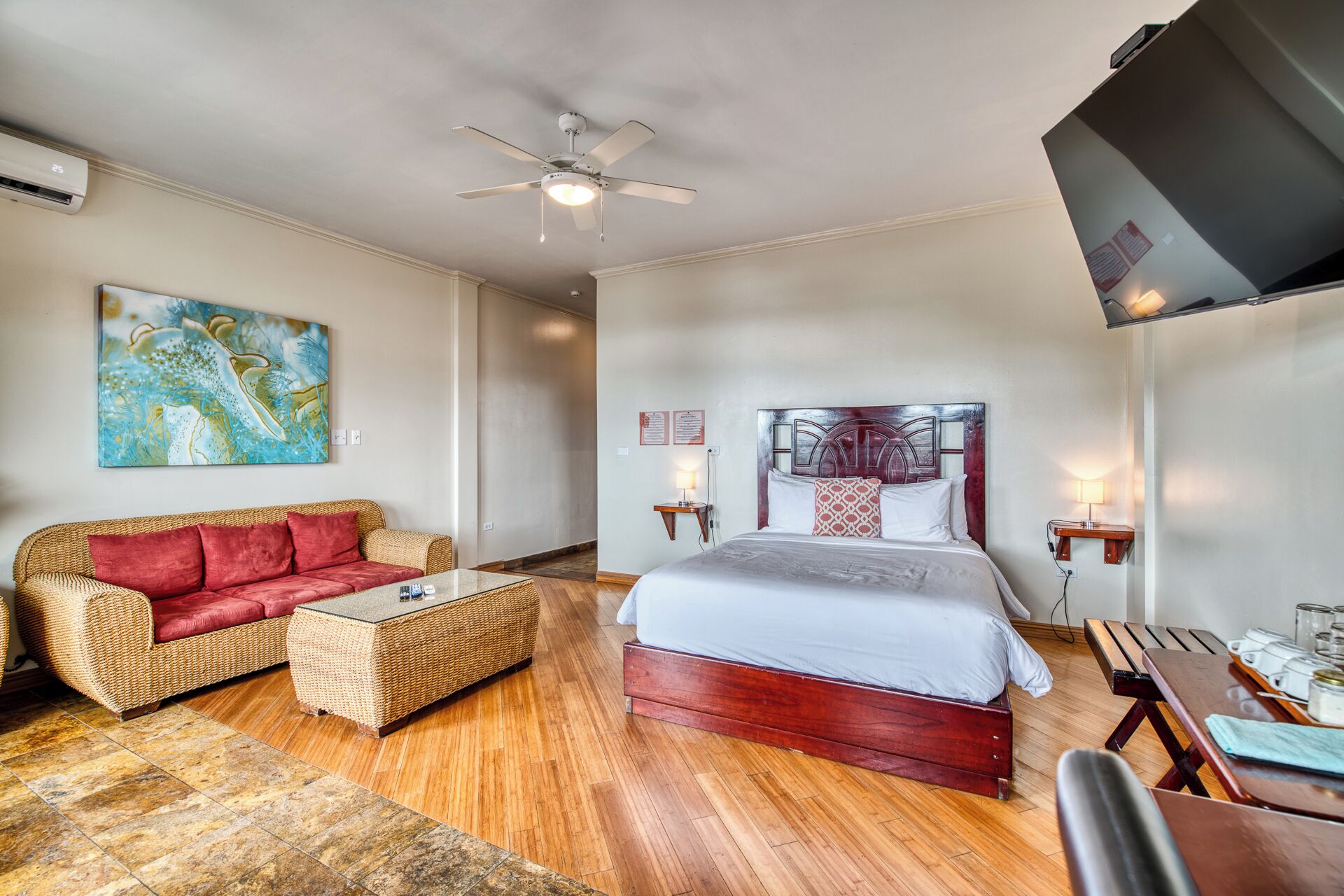 A hotel room with a bed, a sofa, a coffee table, a ceiling fan, and a painting on the wall.