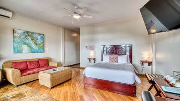 A hotel room with a bed, a sofa, a coffee table, a ceiling fan, and a painting on the wall.