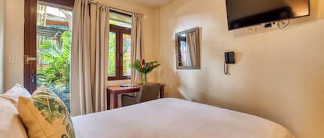 A hotel room with a bed, a desk with a chair, a telephone, a television, and a window with curtains.
