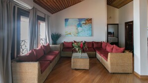 A living room with a wooden ceiling, wicker sofas, a coffee table, and a large abstract painting on the wall.