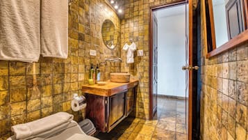 A bathroom with a stone wall, a wooden vanity, a toilet, and a door leading to another room.