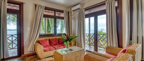 A spacious living area with a sofa, a glass coffee table, and a view of the sea through large windows.