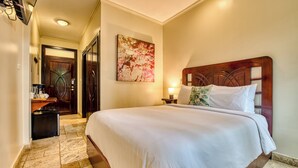 Una habitación de hotel con una cama grande, un cabecero de madera, una mesita de noche con una lámpara y un cuadro en la pared.