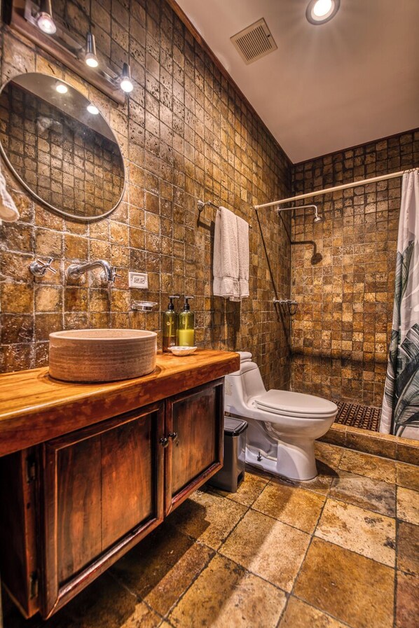 A bathroom with a round sink, wooden vanity, a toilet, and a shower area with a tiled wall. - Hotel Palma Royale (Bocas del Toro)