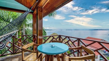 A wooden deck with a round table and chairs, overlooking a body of water with a clear sky.
