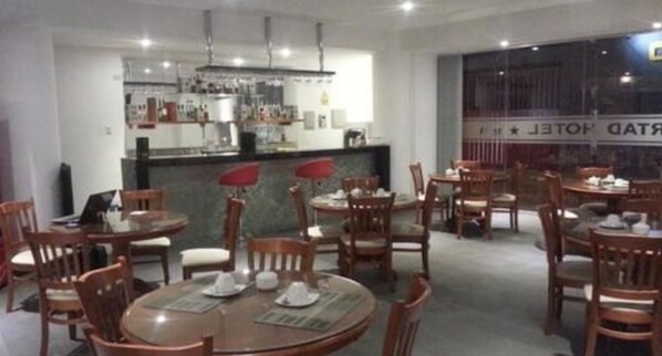 Un restaurante con mesas y sillas redondas, una zona de bar y vistas a la calle.