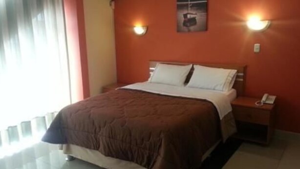 A hotel room with a bed, a nightstand with a phone, and two wall-mounted lights. - Hotel Libertad (Trujillo)