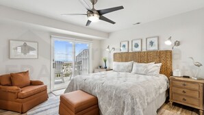 A bedroom with a bed, a nightstand, a chair, a ceiling fan, and a window with a view of buildings.