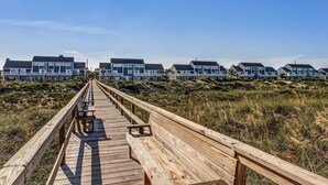 A wooden boardwalk leading to a row of beach houses with large windows and white railings.