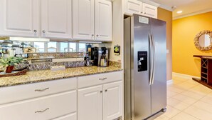 Una cocina con armarios blancos, un refrigerador de acero inoxidable, una encimera de granito y una cafetera.