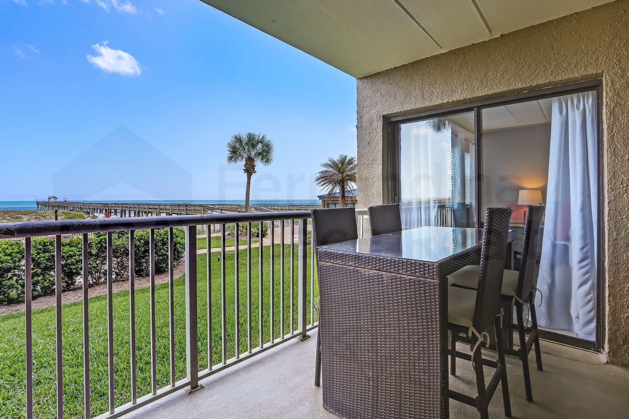 Ein Balkon mit Tisch und Stühlen, Blick auf den Strand und eine Palme.
