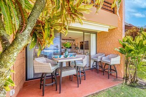 An outdoor patio with wicker furniture, a glass door leading to a room, and a view of the surrounding area.
