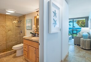 A modern bathroom with a shower, toilet, and vanity. There is a framed artwork on the wall and a view of the ocean through large windows.