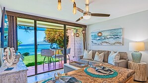 A modern living room with a large window overlooking the ocean, a ceiling fan, and a dining area with a view.