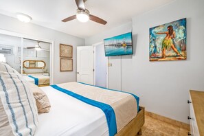 A bedroom with a bed, a ceiling fan, a painting, and a door.
