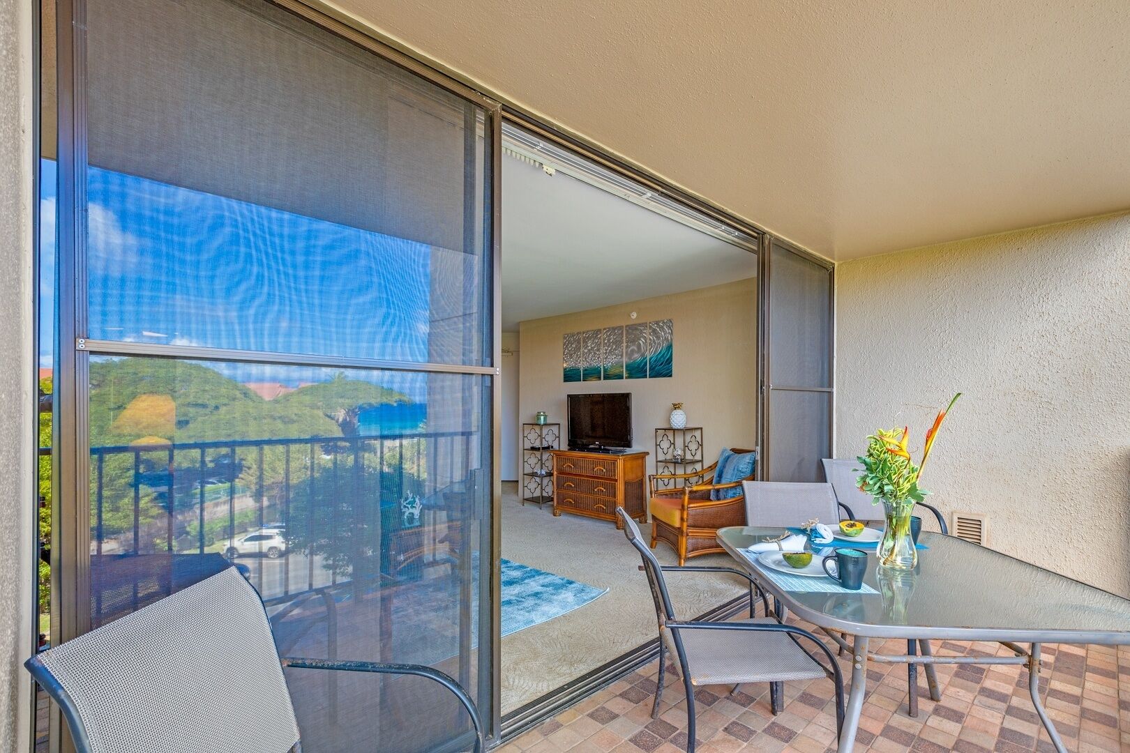 Un balcon avec une porte-fenêtre, une table à manger avec des chaises, un téléviseur et un canapé.