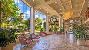 A spacious lobby with large windows, tropical plants, and a patterned stone floor.