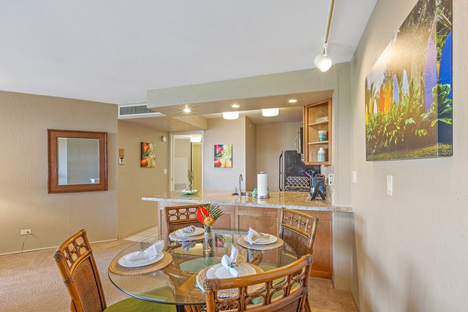 A dining area with a glass-top table, wooden chairs, and a kitchen in the background.