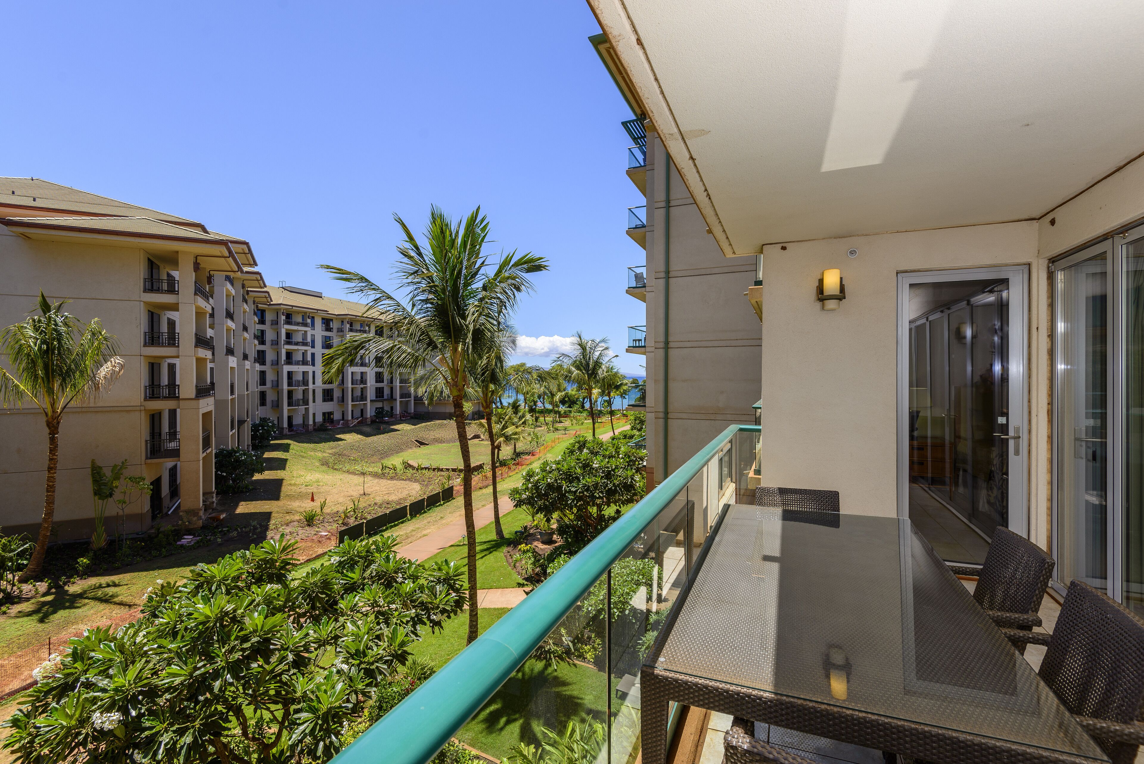 Ein Balkon mit Glastisch und Stühlen, der auf einen Innenhof mit Palmen und einem Gebäudekomplex blickt.