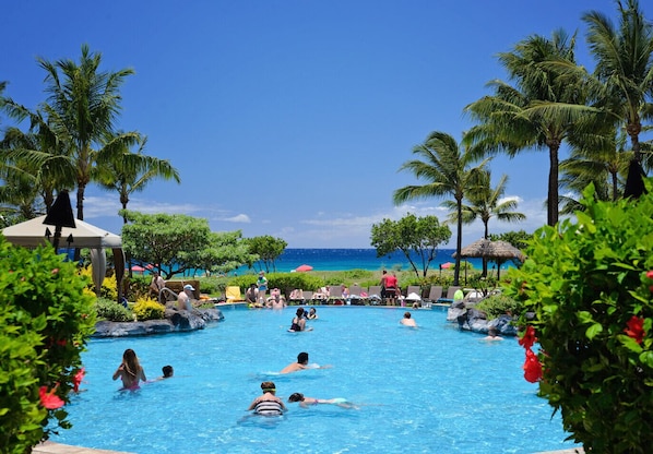 Relax by the pool surrounded by lush greenery and palm trees, with the ocean view in the background.