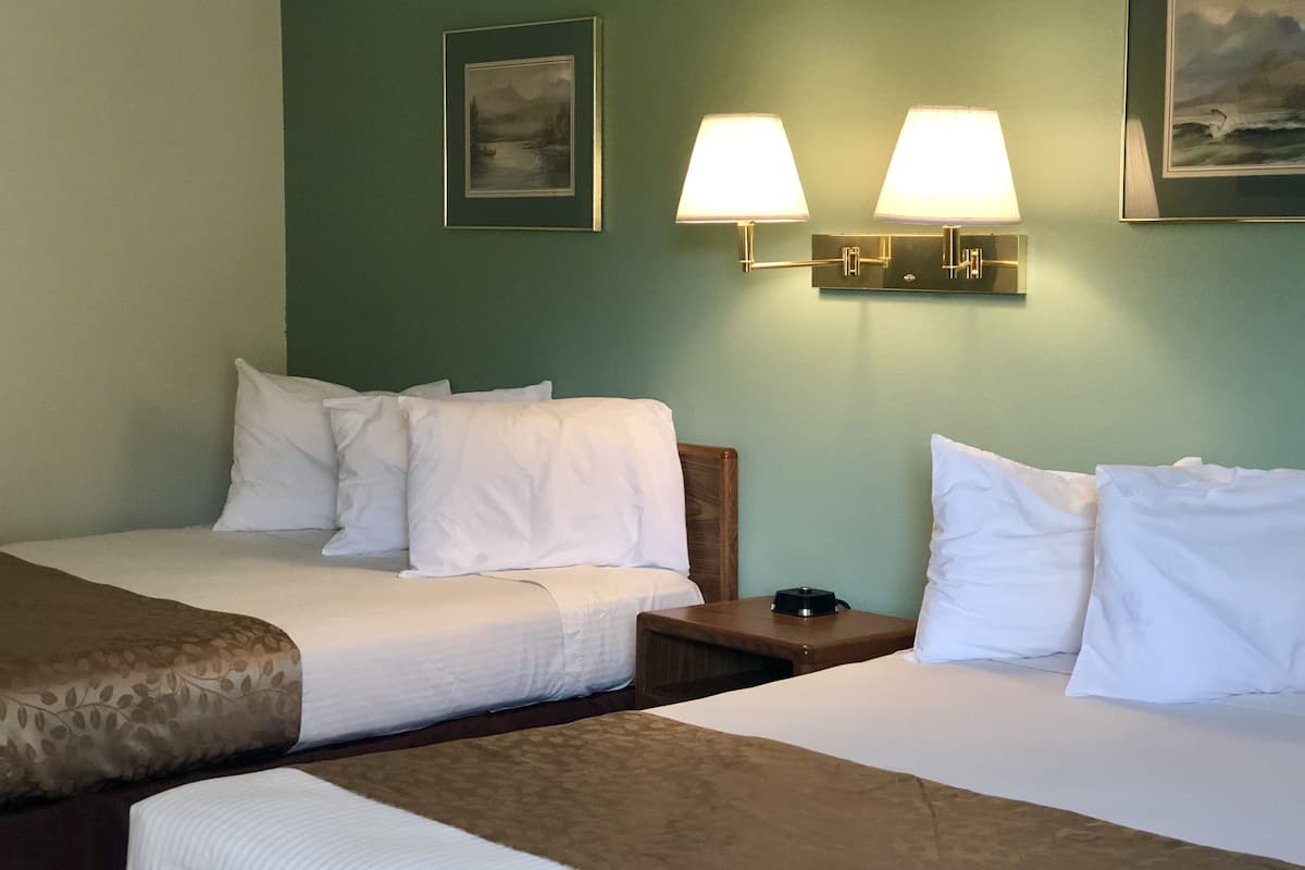 A hotel room with two beds, a nightstand, and wall-mounted lamps.