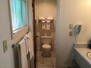 A bathroom with a toilet, a towel rack with towels, a hairdryer, and a window with blinds. - Golden Eagle Inn (Jackson)