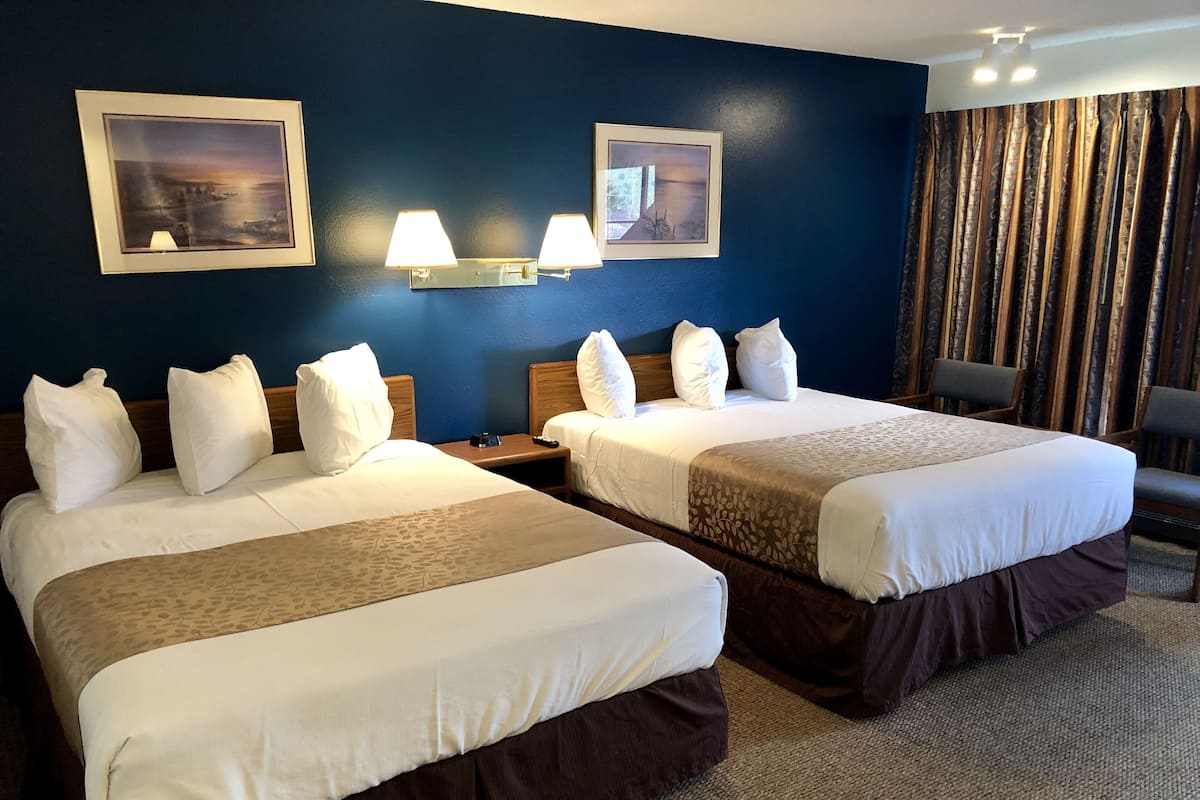 A hotel room with two beds, a nightstand, a lamp, and a chair.
