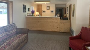 A reception area with a wooden counter, a sofa, and a red armchair. - Golden Eagle Inn (Jackson)