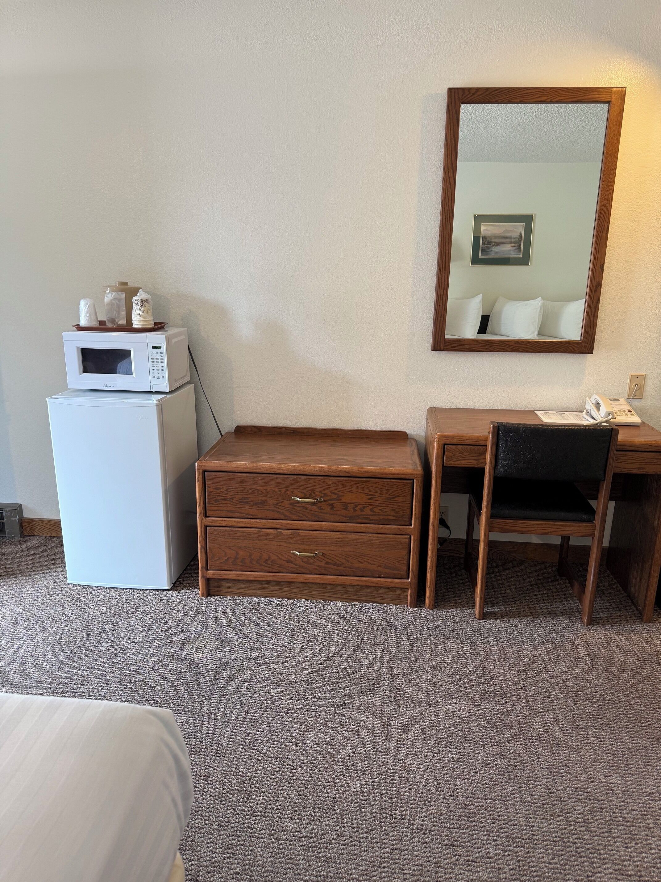 Habitación de hotel con microondas, refrigerador, escritorio de madera, silla y un espejo grande en la pared.