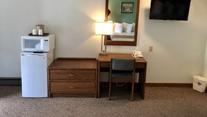 A hotel room with a desk, a microwave, a refrigerator, a lamp, a telephone, a TV, and a trash can. - Golden Eagle Inn (Jackson)