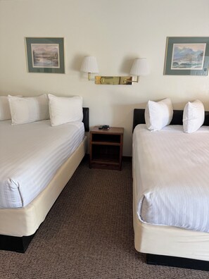 Habitación de hotel con dos camas, una mesita de noche y dos lámparas de pared.