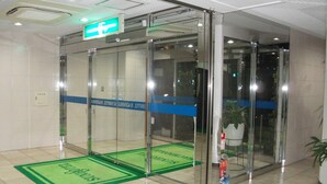 A glass elevator entrance with a green mat and a sign above it. - Sun Hotel Hachioji (Hachioji)
