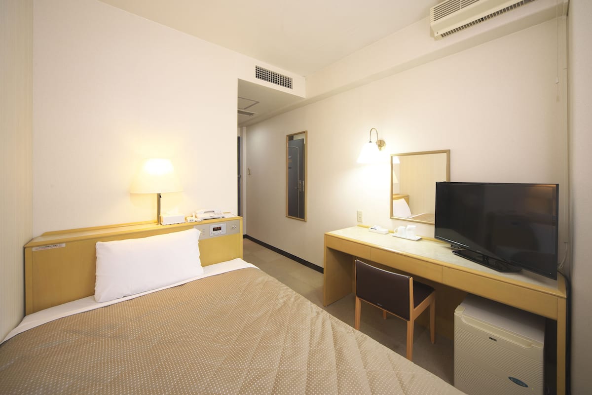 Una camera d'albergo con un letto, una scrivania, una sedia, una televisione e un piccolo frigorifero.