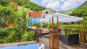Una terraza de madera con mobiliario exterior, piscina y un edificio de diseño moderno.