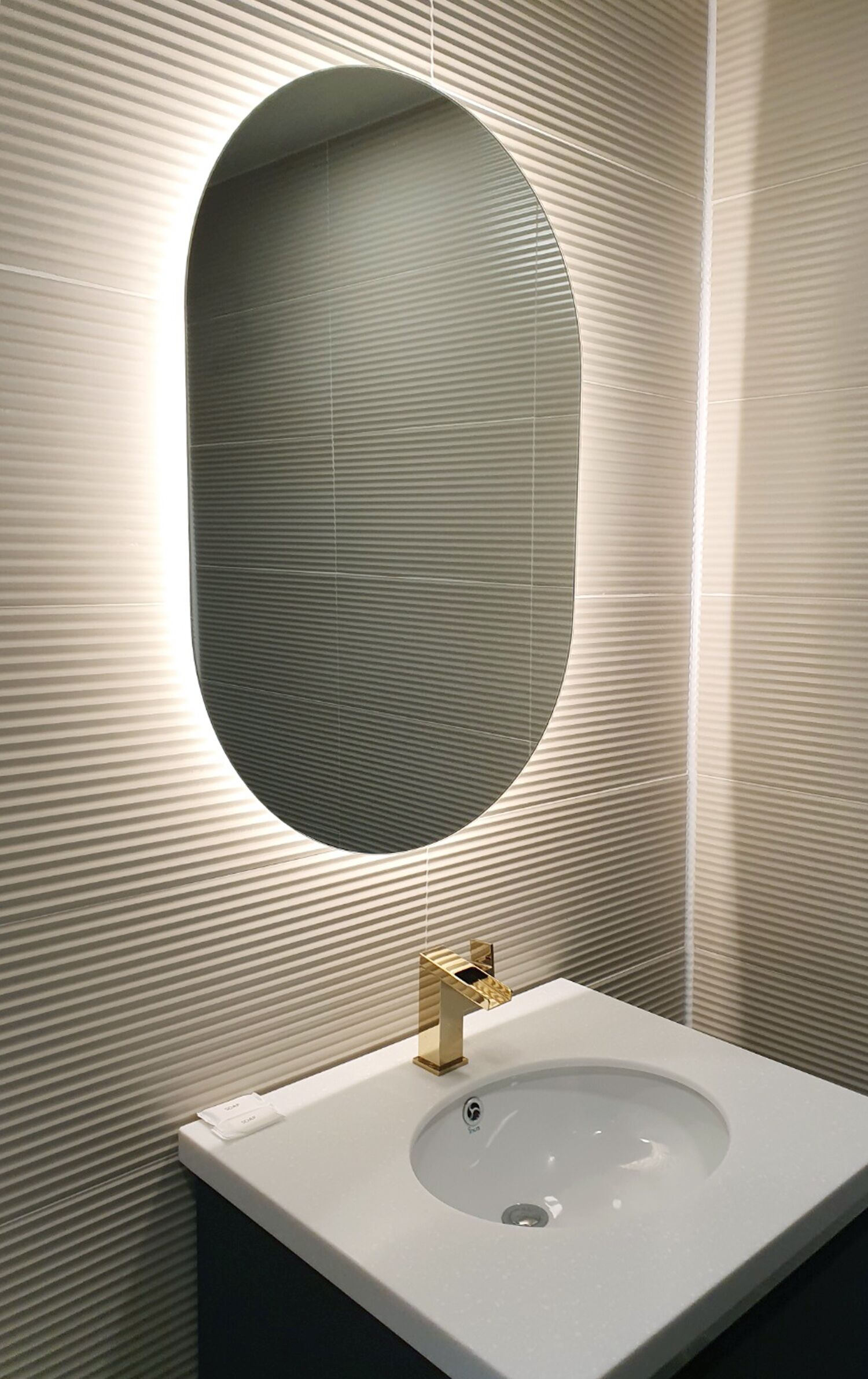 A bathroom with a white sink, a gold faucet, and a large oval mirror.