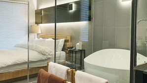 Una habitación de hotel moderna con una cama grande, cabina de ducha con paredes de vidrio y un área de baño separada.