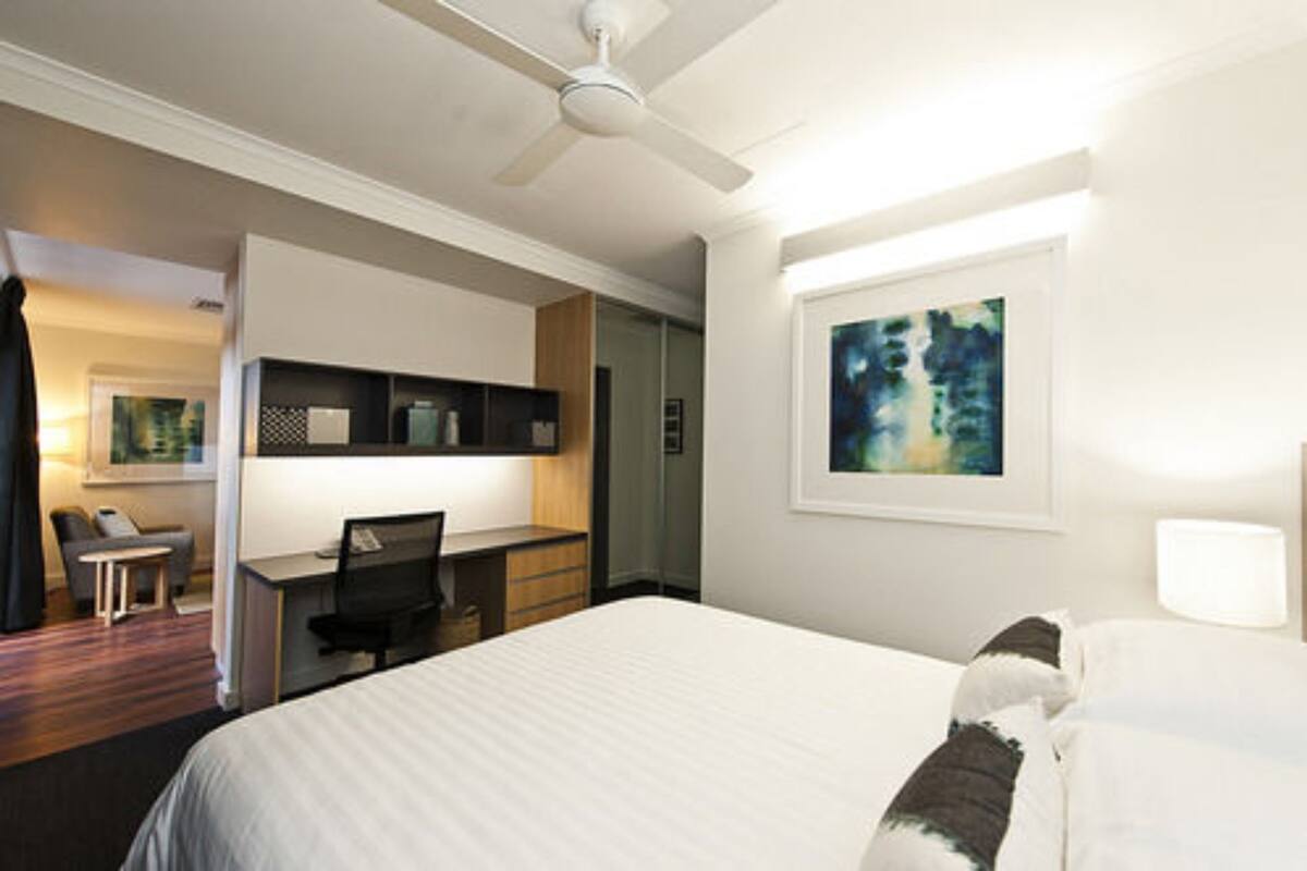 Una habitación de hotel con cama, escritorio, silla y un cuadro en la pared.