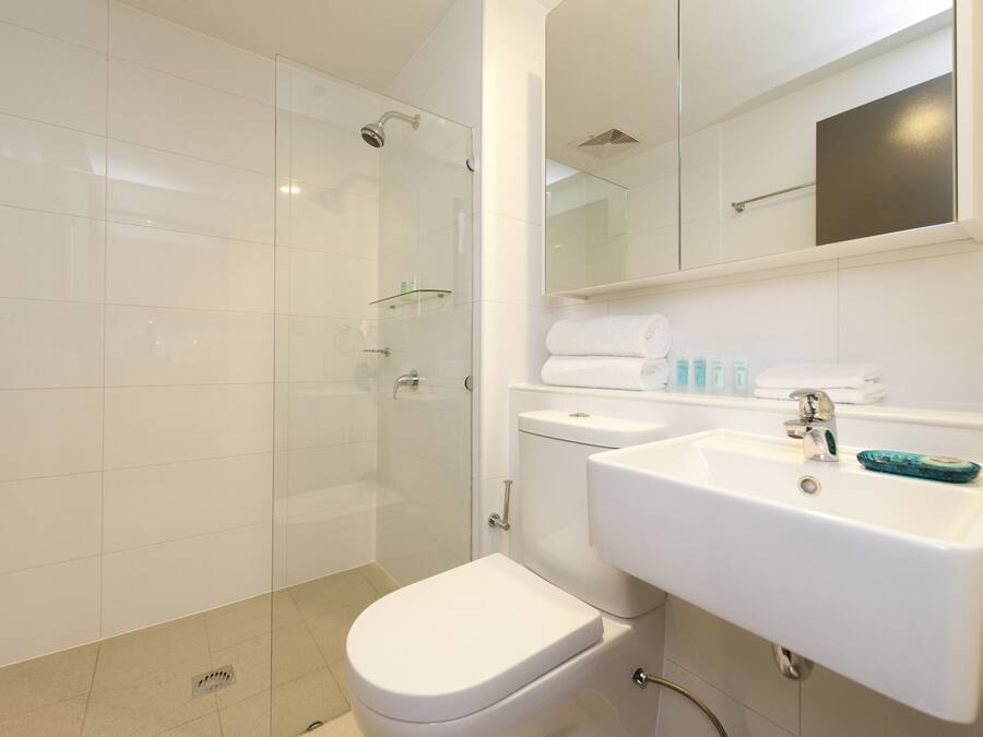 Un baño moderno con ducha de vidrio, inodoro blanco y lavabo con espejo.