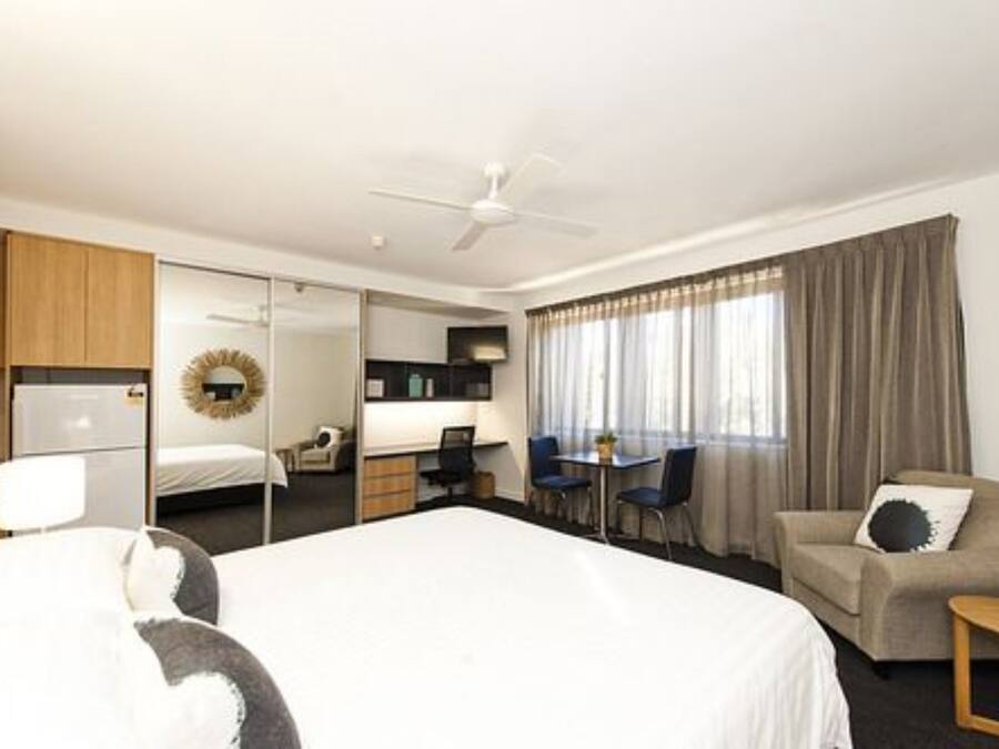 Habitación de hotel con una cama grande, un escritorio con sillas, un sofá y un ventilador de techo.