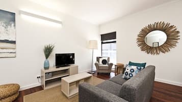 Una sala de estar moderna con un sofá gris, un televisor de pantalla plana, una lámpara y un espejo decorativo.