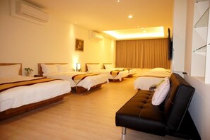 Habitación de hotel con cuatro camas individuales, un sofá y una televisión montada en la pared.