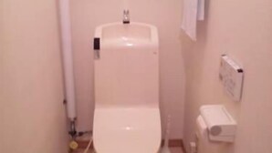 A small, white toilet with a tank and a flush handle, a white towel hanging on the wall, and a white electrical outlet.