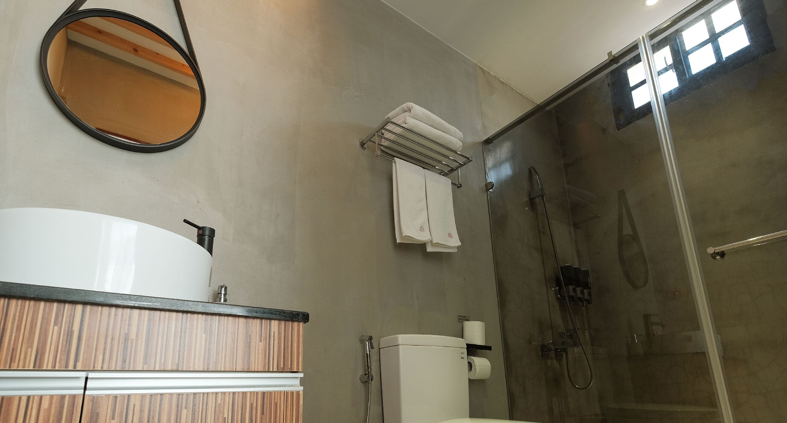 Un baño con tocador de madera, lavamanos blanco, inodoro, cabina de ducha de vidrio y espejo.