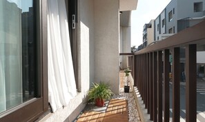 A narrow outdoor corridor with a wooden deck, potted plants, and a metal railing.