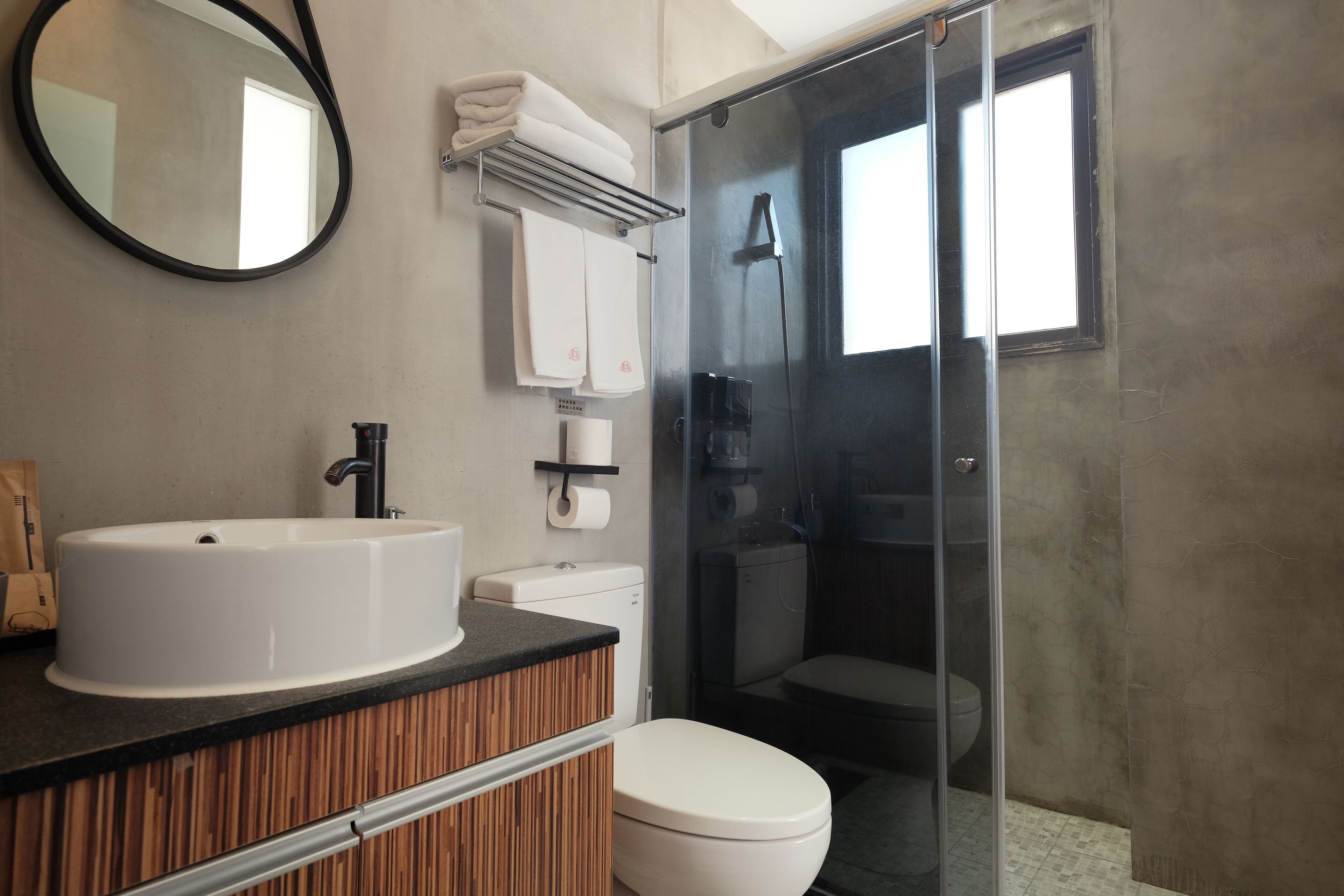 A modern bathroom with a round mirror, a white sink, a toilet, and a glass shower enclosure.