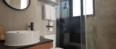 A modern bathroom with a round mirror, a white sink, a toilet, and a glass shower enclosure.