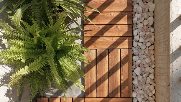 Una terraza de madera con un macetero de helechos verdes y una capa de guijarros blancos.