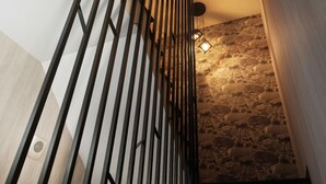 Una escalera con barandilla de diseño moderno, una pared de piedra con textura y un aplique de pared.